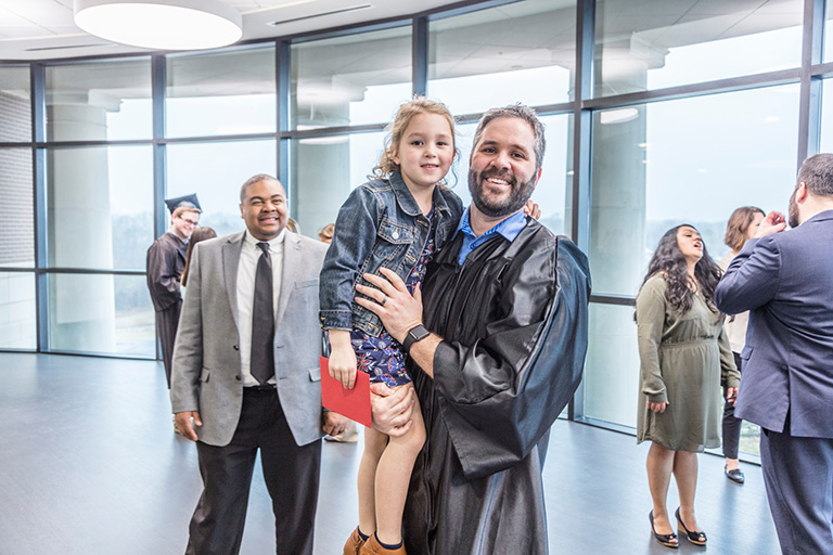Father graduating, holding daughter in his arms