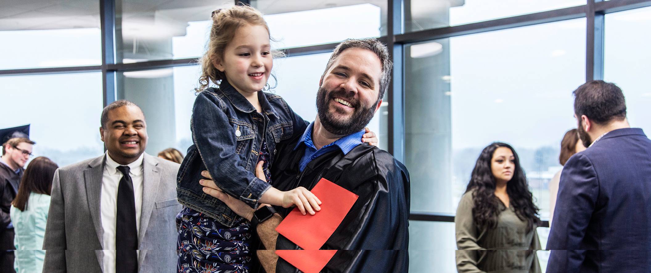 Graduate dad holds young daughter on graduation day