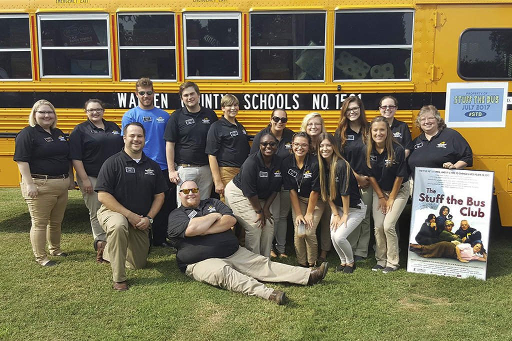 group of people posing in front of a school bus