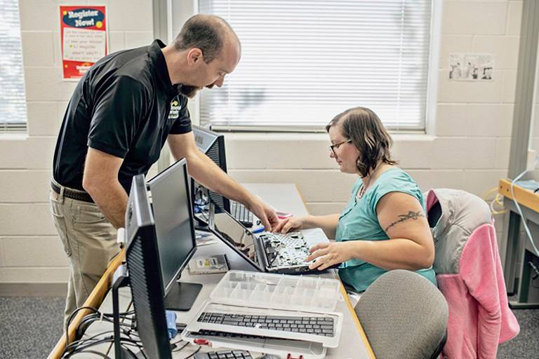 Instructor helping student take a computer apart. 