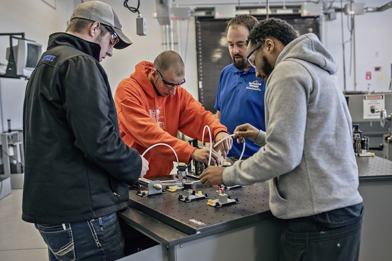 four men around table working with tubing and industrial equipment