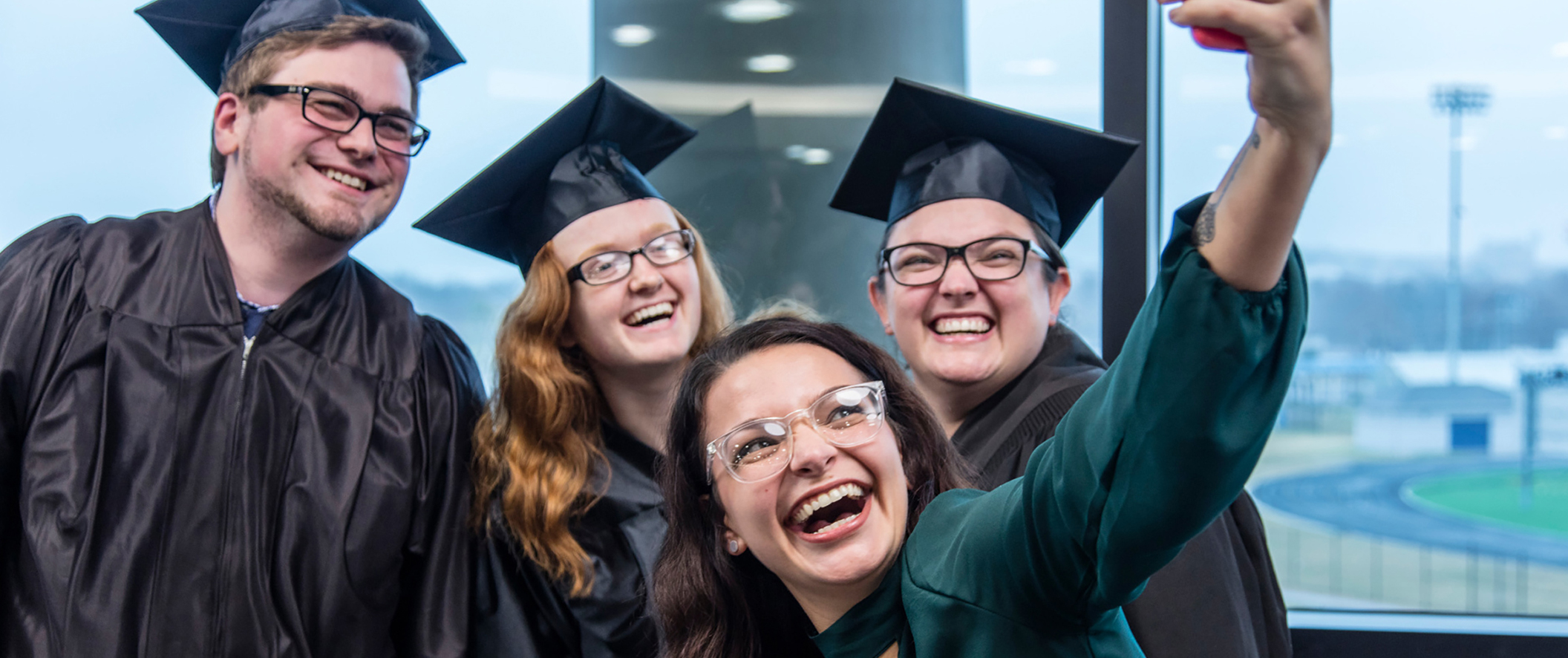 Three graduates and a friend taking a selfie on a cell phone