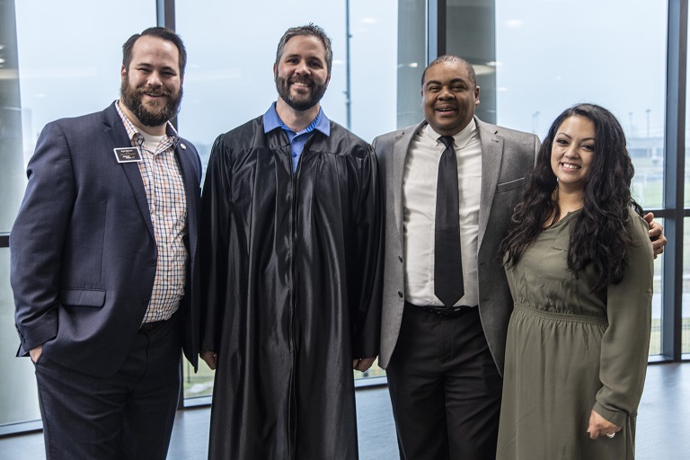 Student in graduation gown posing with two men in suits and a woman in a dress