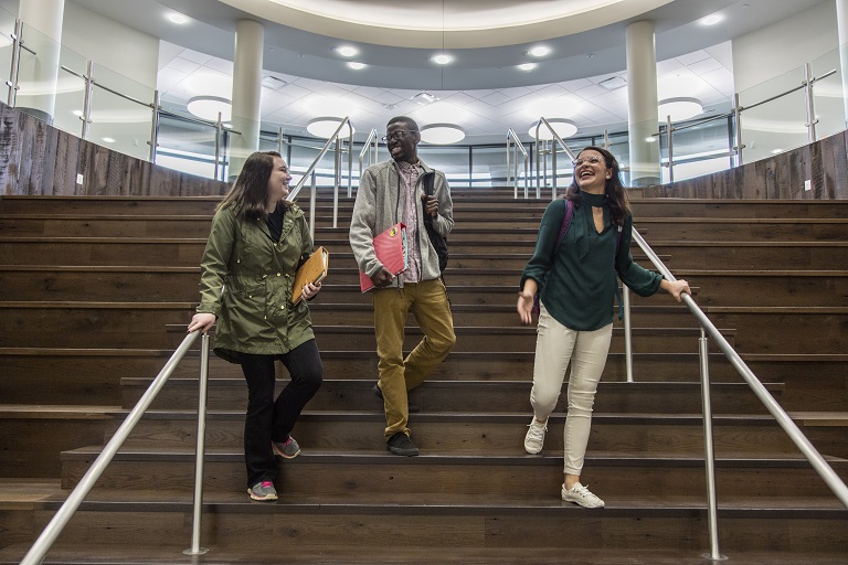 Three students laughing while chatting and walking down steps