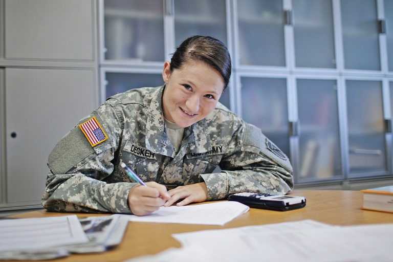 woman in military uniform smiling at the camera while writing on a paper