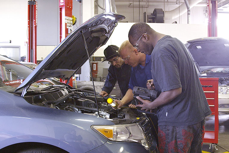 Students working on a car while the instructor helps them.