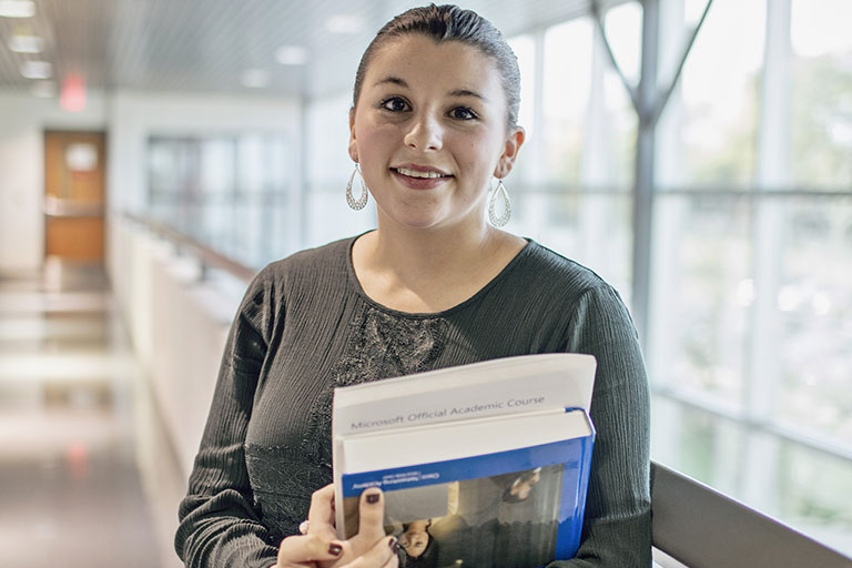 Student standing in hallway holding a book. 