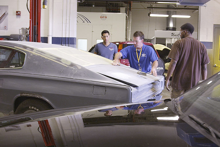 Instructor demonstrating to students how to sand a car. 