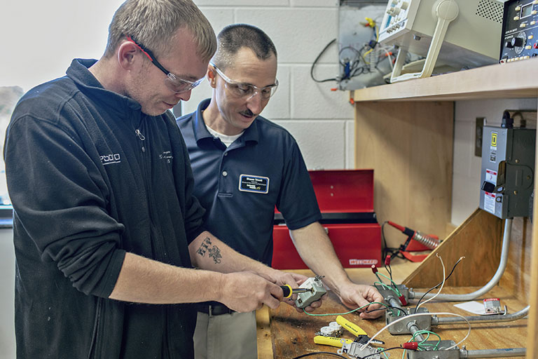 Instructor watching student wire a plug. 