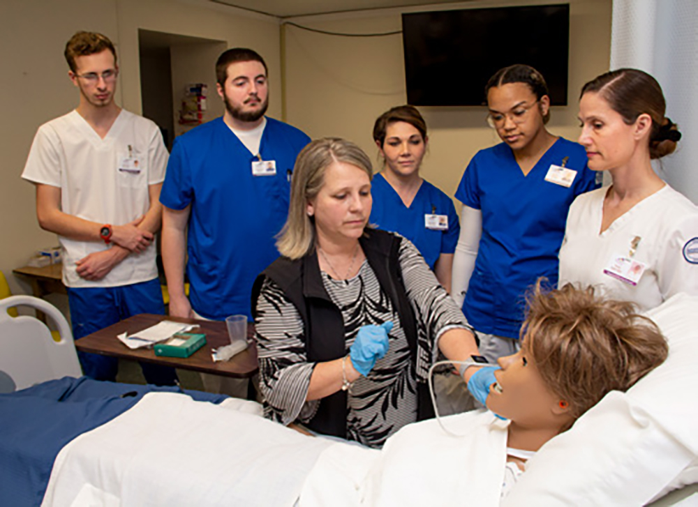 Dr. Angie Harlan instucting at a bedside in the medical lab with students watching