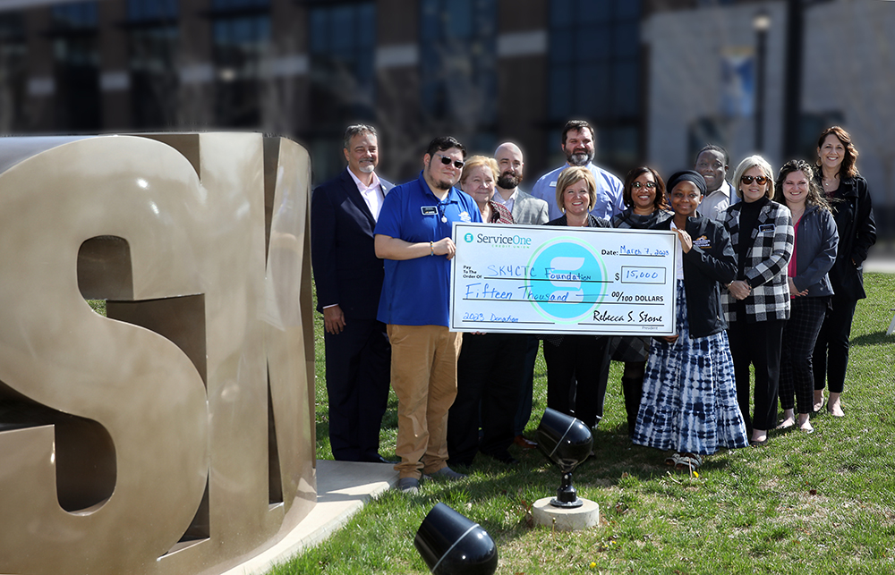 group of peoplefrom Service One Credit Union and SKYCTC standing beside SKY Sculpture presenting check.