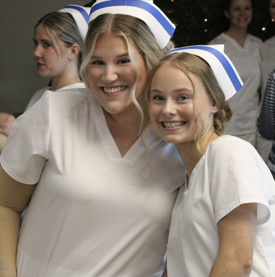 Two female nursing students in uniform hugging for photo.