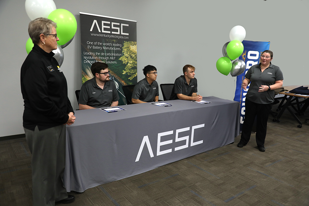 Five people standing and setting at a table ready to sign going pro agreements.