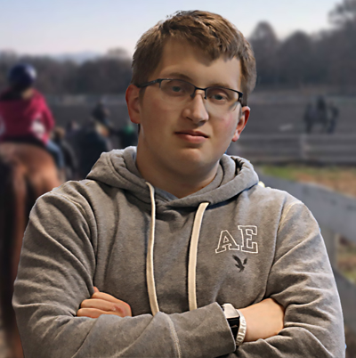 Joshua Martin with arms crossed and student riding horses in the background