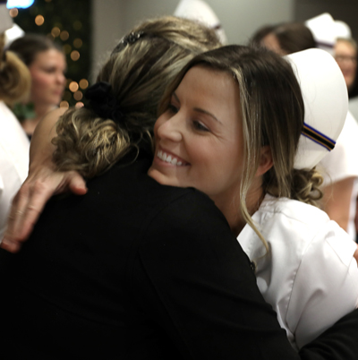 Nursing student in uniform at nursing graduation hugging her mother.