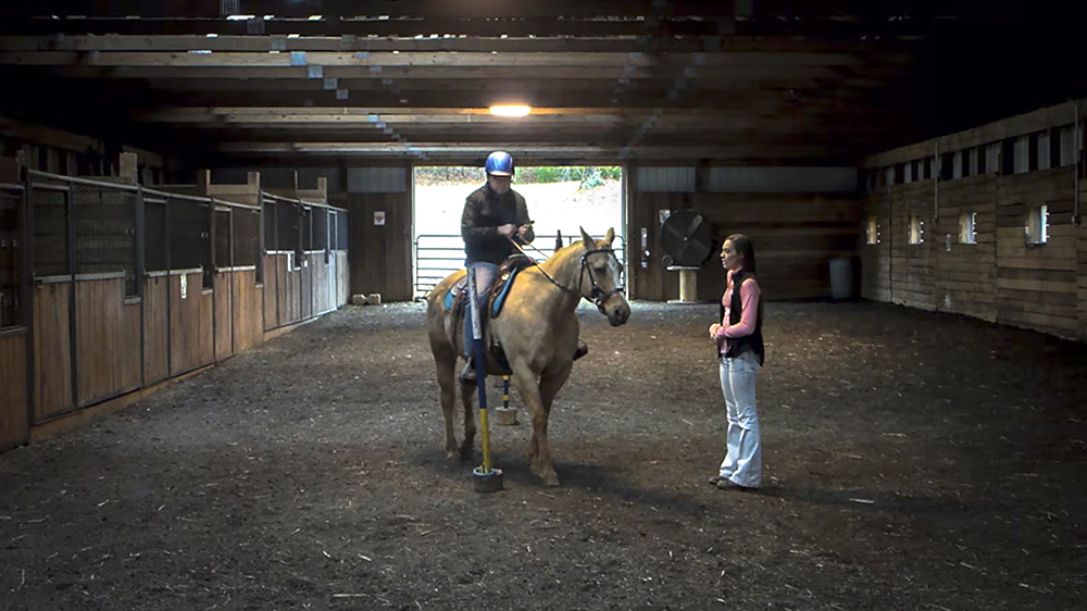 Male on a horse in a riding stable with female standing next to horse