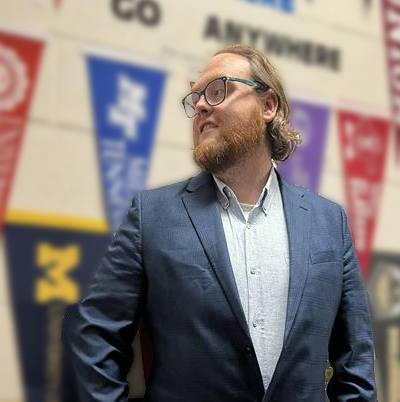 Travis Hardin standing in front of various college and university pennants. 