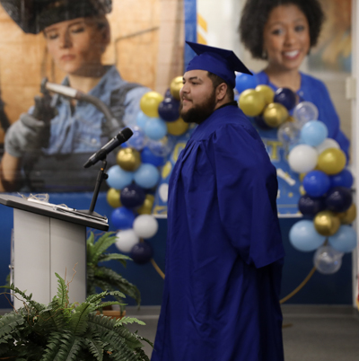 Man standing talking to audience in cap and gown