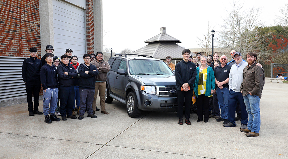 Large group of students, faculty and business leaders standing around a donation automobile