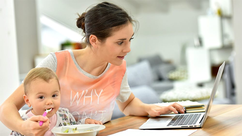 Female student working on her laptop holding infant