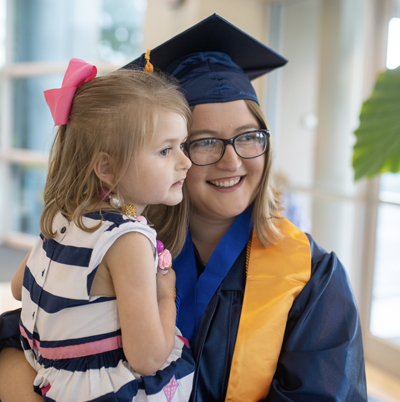 Female graduate in cap and gown holding a child