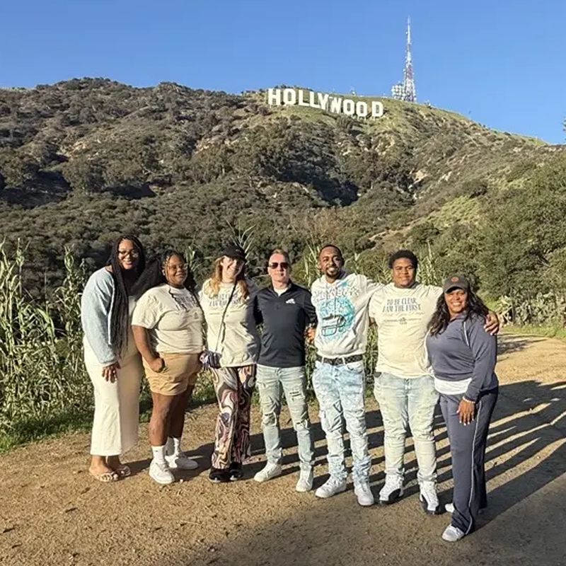 Seven students standing in field with Hollywood sign in background.
