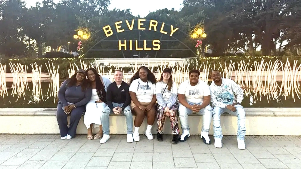 Seven students setting on a bench in front of the Beverly Hillis sign