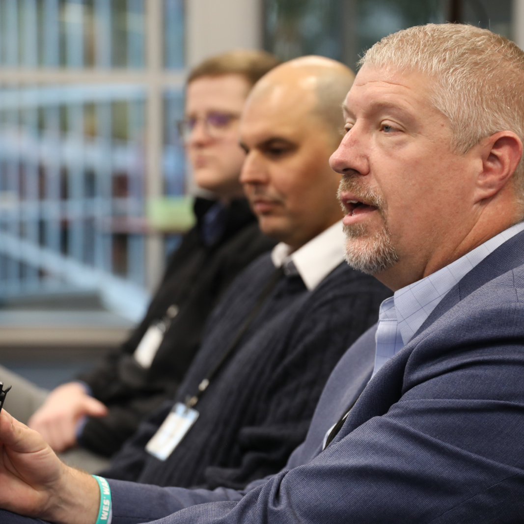 Three men on a panel speaking to audience. 