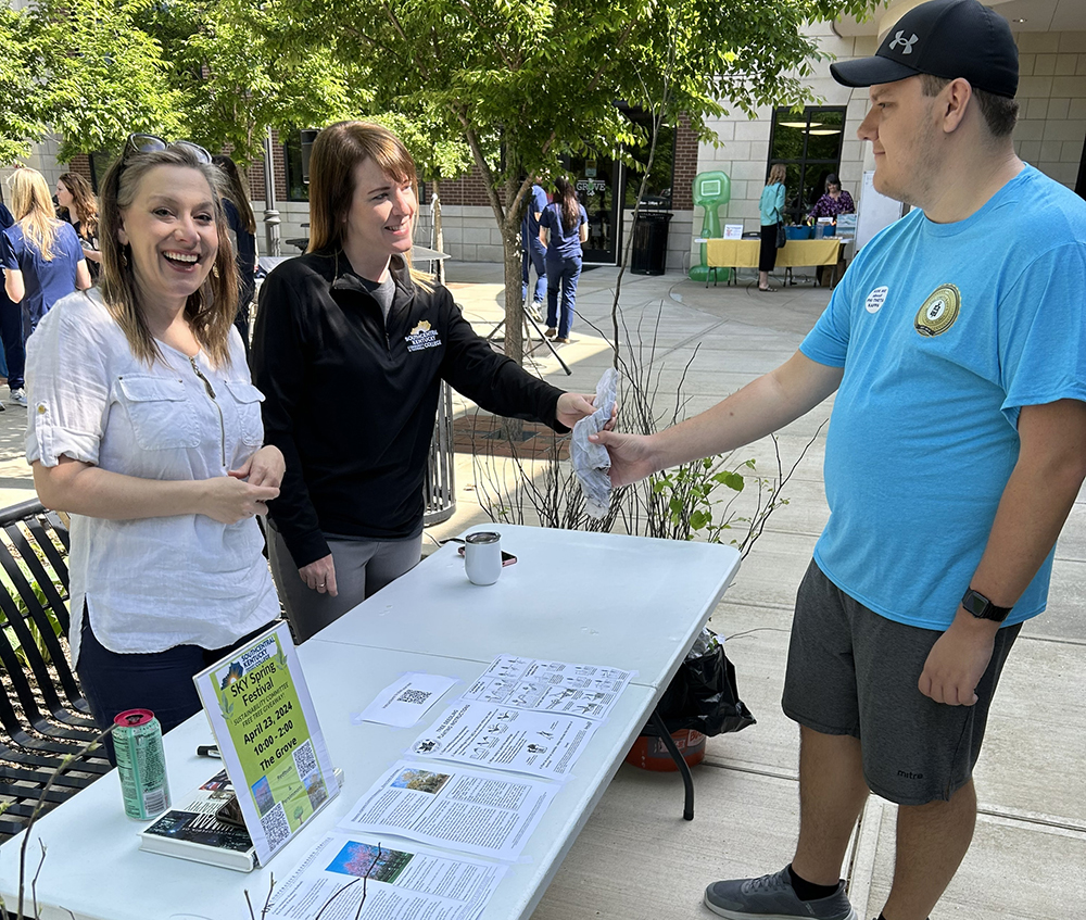 Two femal SKYCTC staff members handing a small tree to a student at the college