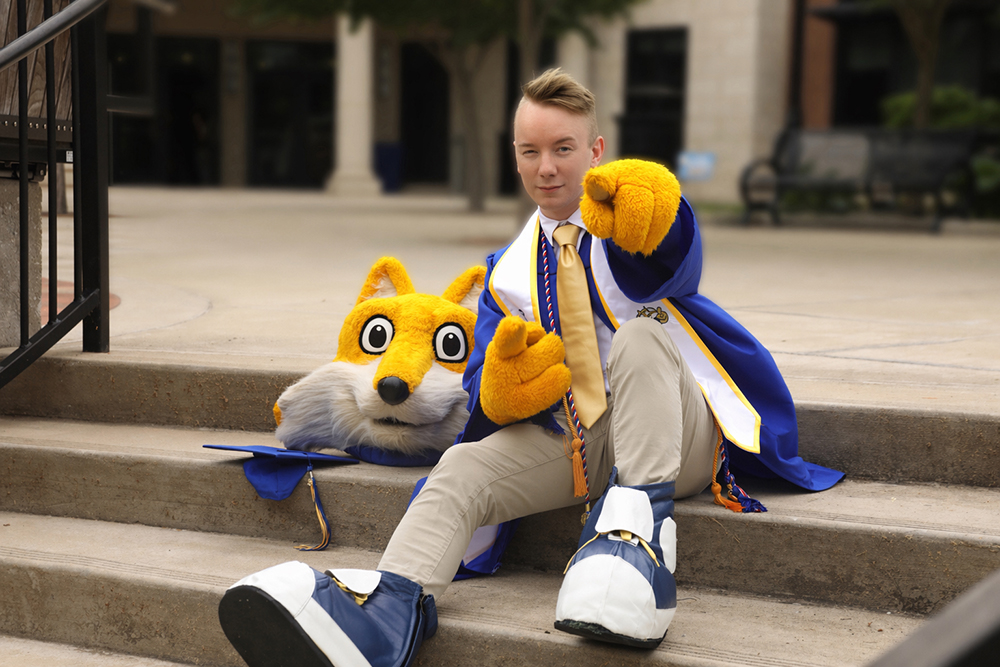 Alex Smith with Pathfinder gloves on and Pathfinder head beside him, setting on college steps