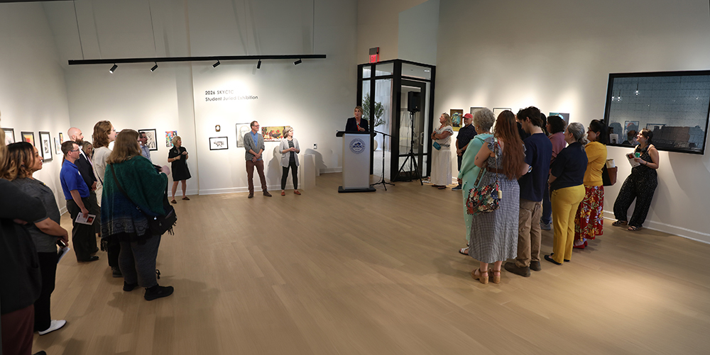 person speaking at art gallery show with people listing.