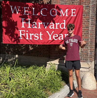 Braden Johnson standing on Harvard campus by sign that says welcome Harvard first year.