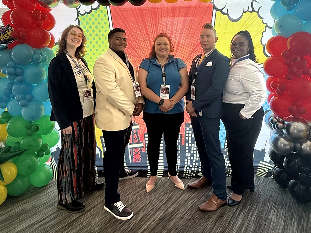 Image of five people from SKYCTC attending the conference in front of a baloon background.