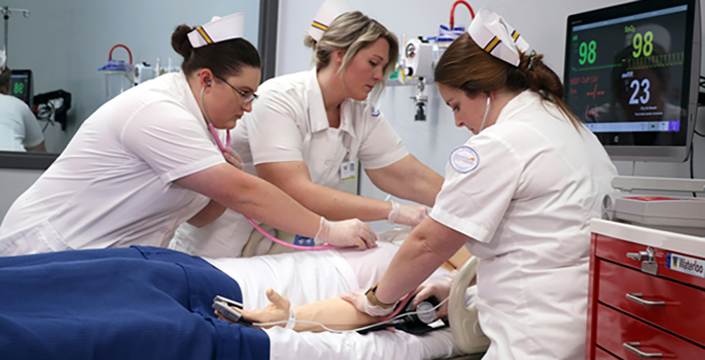 Three female nursing students in uniform in lab working on patient simulation