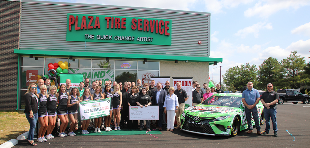 Large groop of people dong a ribbon cutting ceremony in from of a New Plaza Tire Center