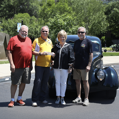 Three men present check to SKYCTC Heather Rogers in front of classic car