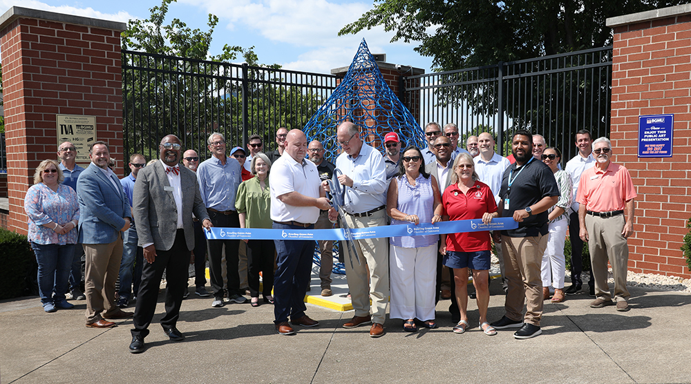 A group of people cutting a ribbon in front of a waterdrop schulpture.