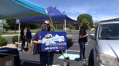 SKYCTC staff members holging sign and giving giftd to graduates in cars
