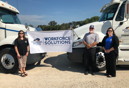 Three people standing in front of CDL trucks with banner saying Workforce Solutions