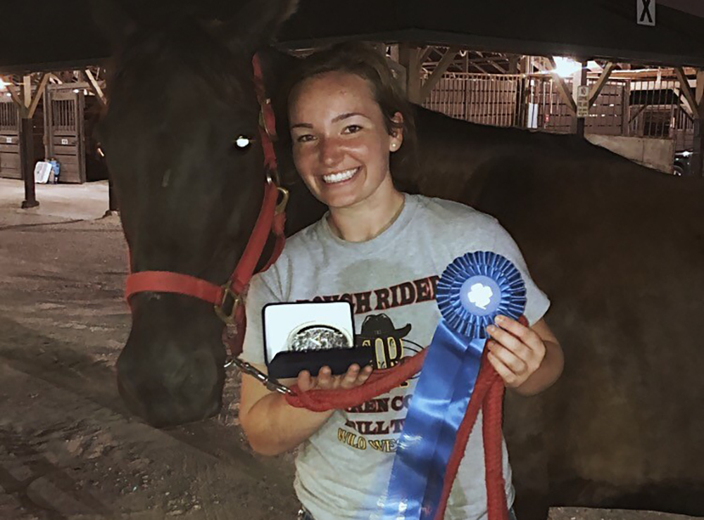 Chloe Carter standing in front of horse with winning ribbons